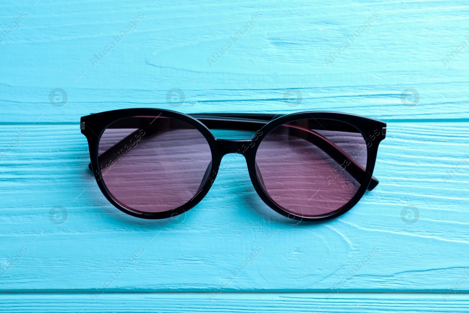 Photo of Stylish sunglasses on light blue wooden background, top view