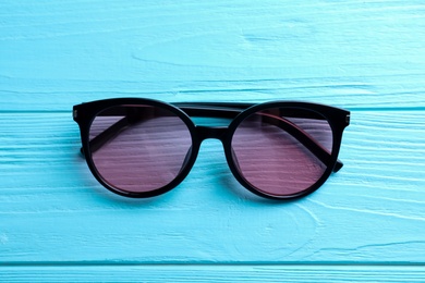 Photo of Stylish sunglasses on light blue wooden background, top view