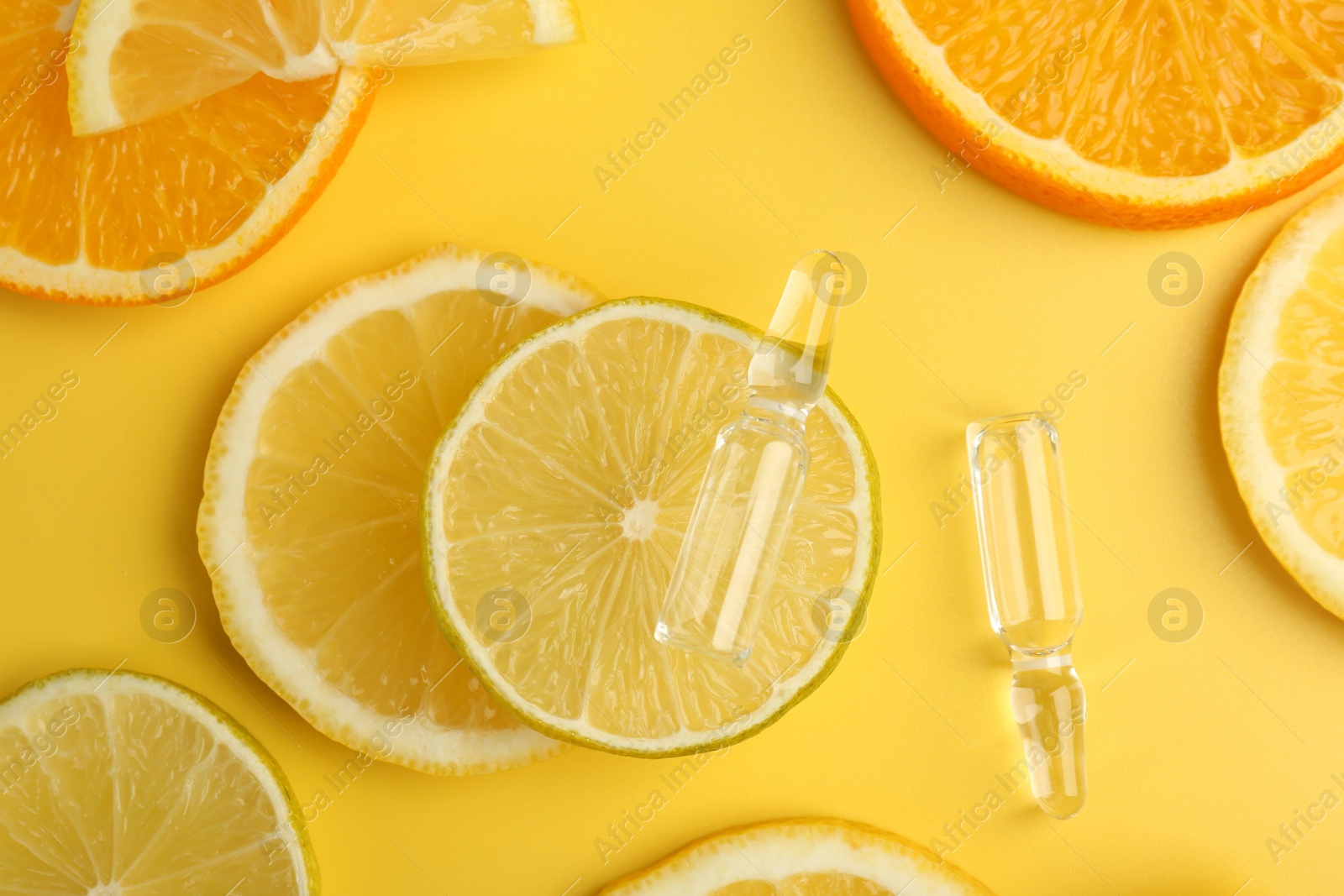 Photo of Skincare ampoules with vitamin C and citrus slices on yellow background, flat lay