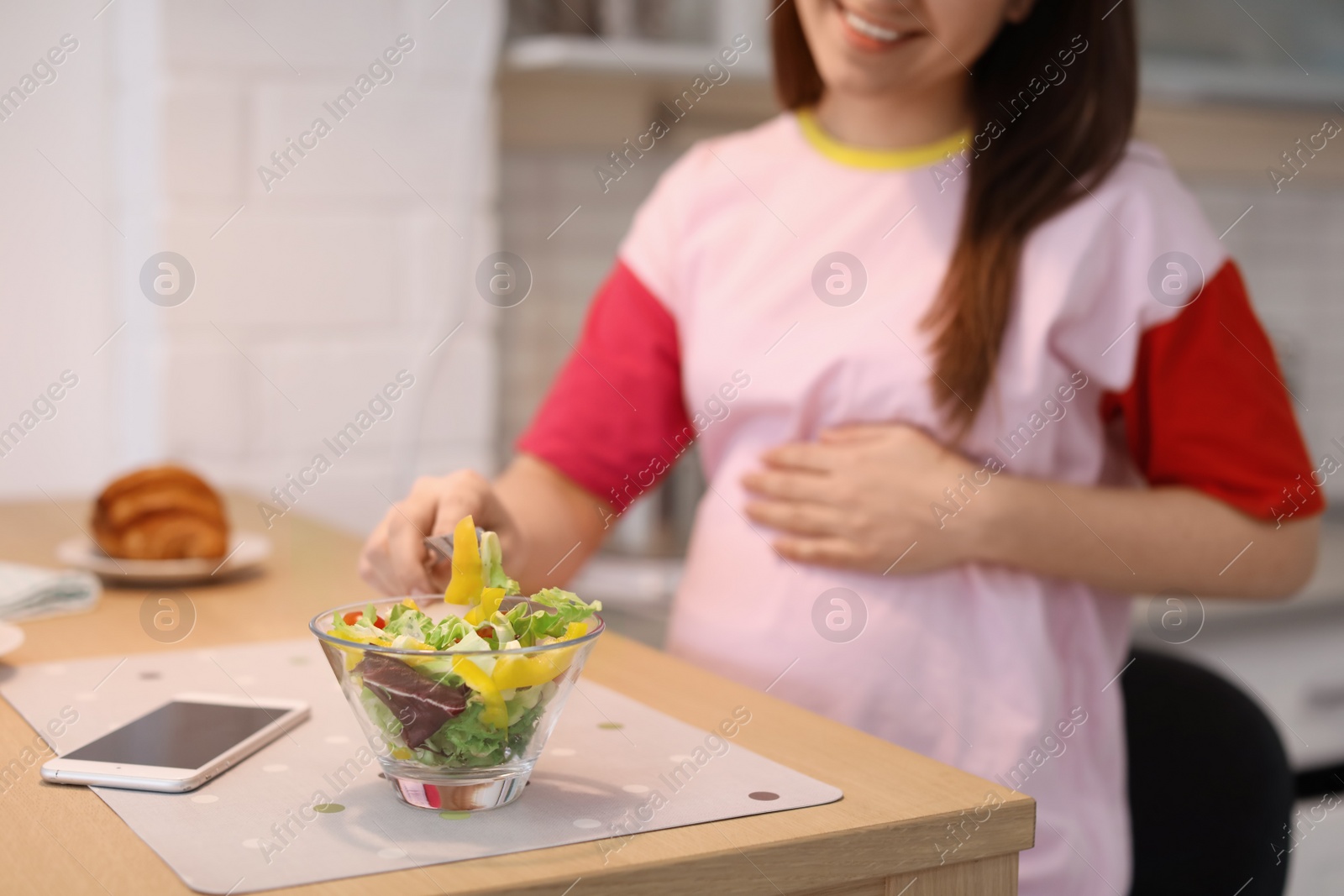 Photo of Young pregnant woman eating vegetable salad at table in kitchen