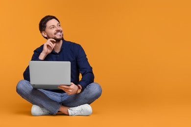 Happy man with laptop sitting on yellow background, space for text