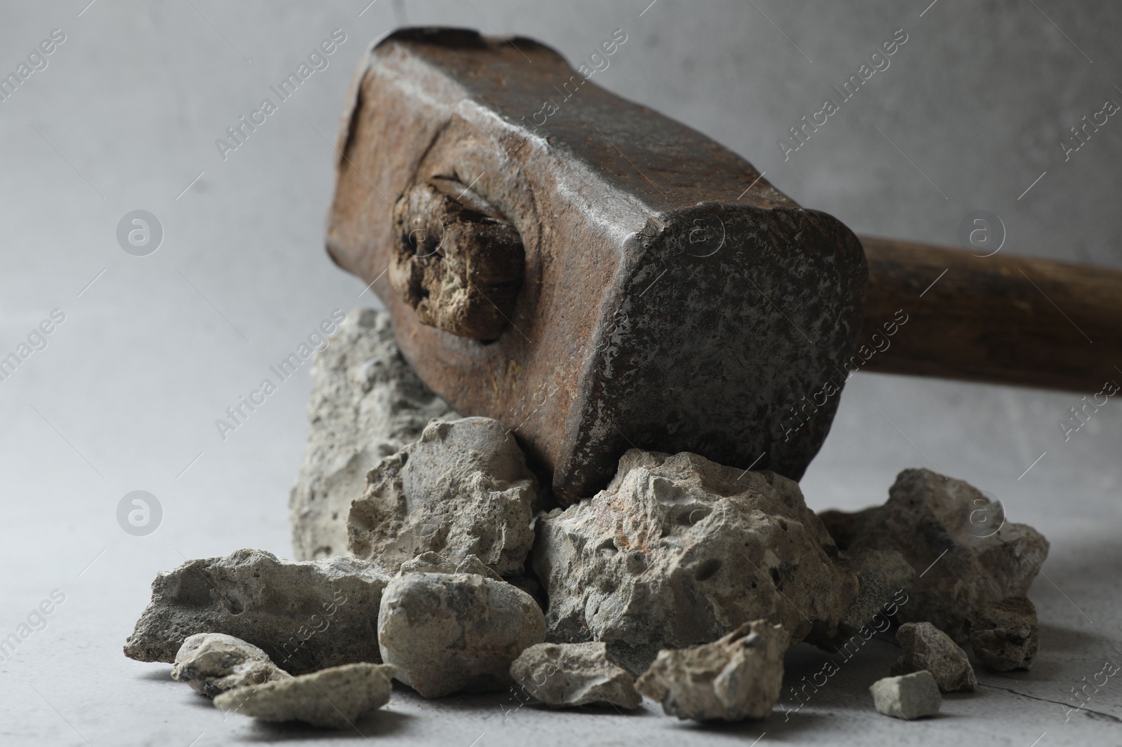 Photo of One sledgehammer and pieces of broken stones on grey background, closeup