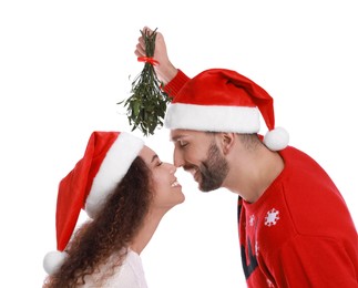 Photo of Lovely couple in Santa hats under mistletoe bunch on white background