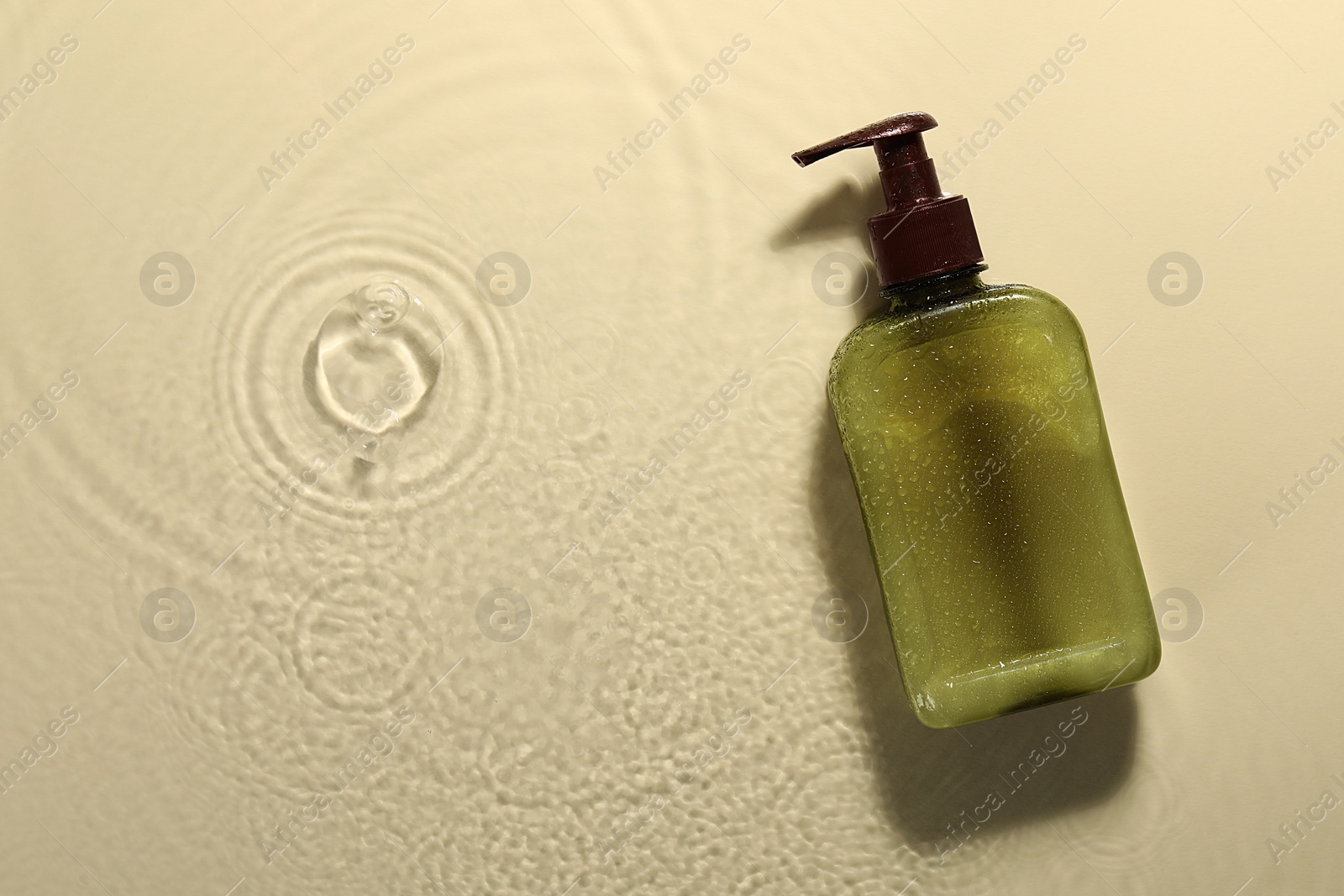 Photo of Bottle of face cleansing product in water against beige background, top view. Space for text