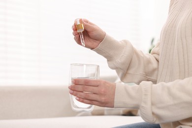 Photo of Woman dripping food supplement into glass of water indoors, closeup. Space for text