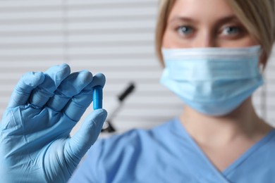 Doctor holding pill on light background, selective focus. Space for text