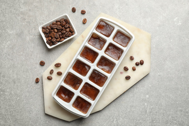 Photo of Ice cubes in tray and coffee beans on grey table, flat lay