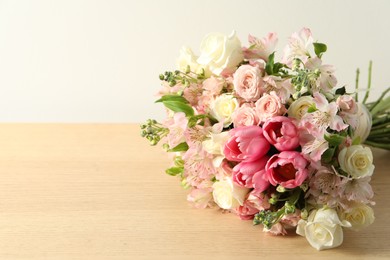 Photo of Beautiful bouquet of fresh flowers on wooden table near light wall. Space for text