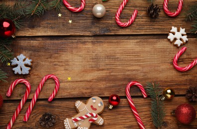 Photo of Frame of tasty candy canes and Christmas decor on wooden table, flat lay. Space for text
