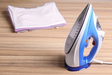 Photo of Modern electric iron and folded clothes on wooden table. Space for text