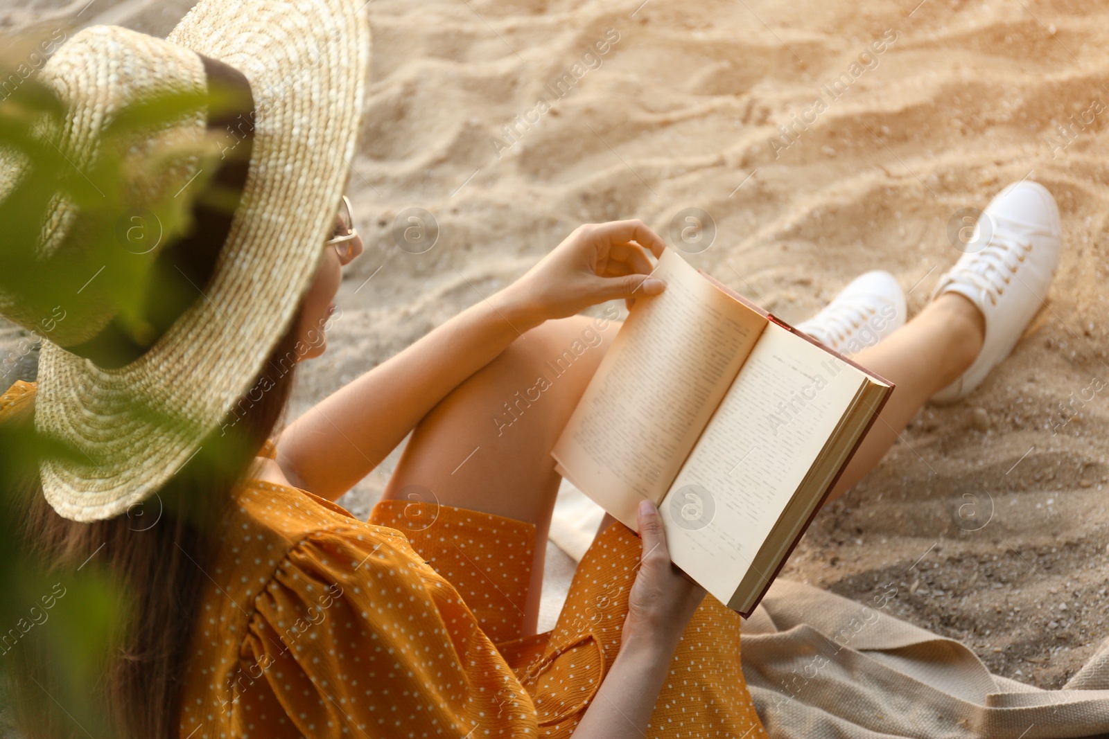 Photo of Young woman reading book on sandy beach