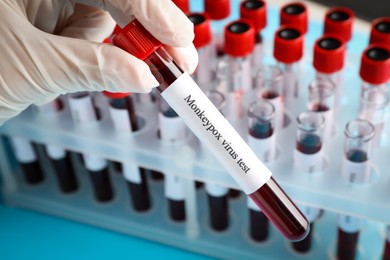 Photo of Monkeypox virus test. Laboratory worker holding sample tube with blood near rack, closeup