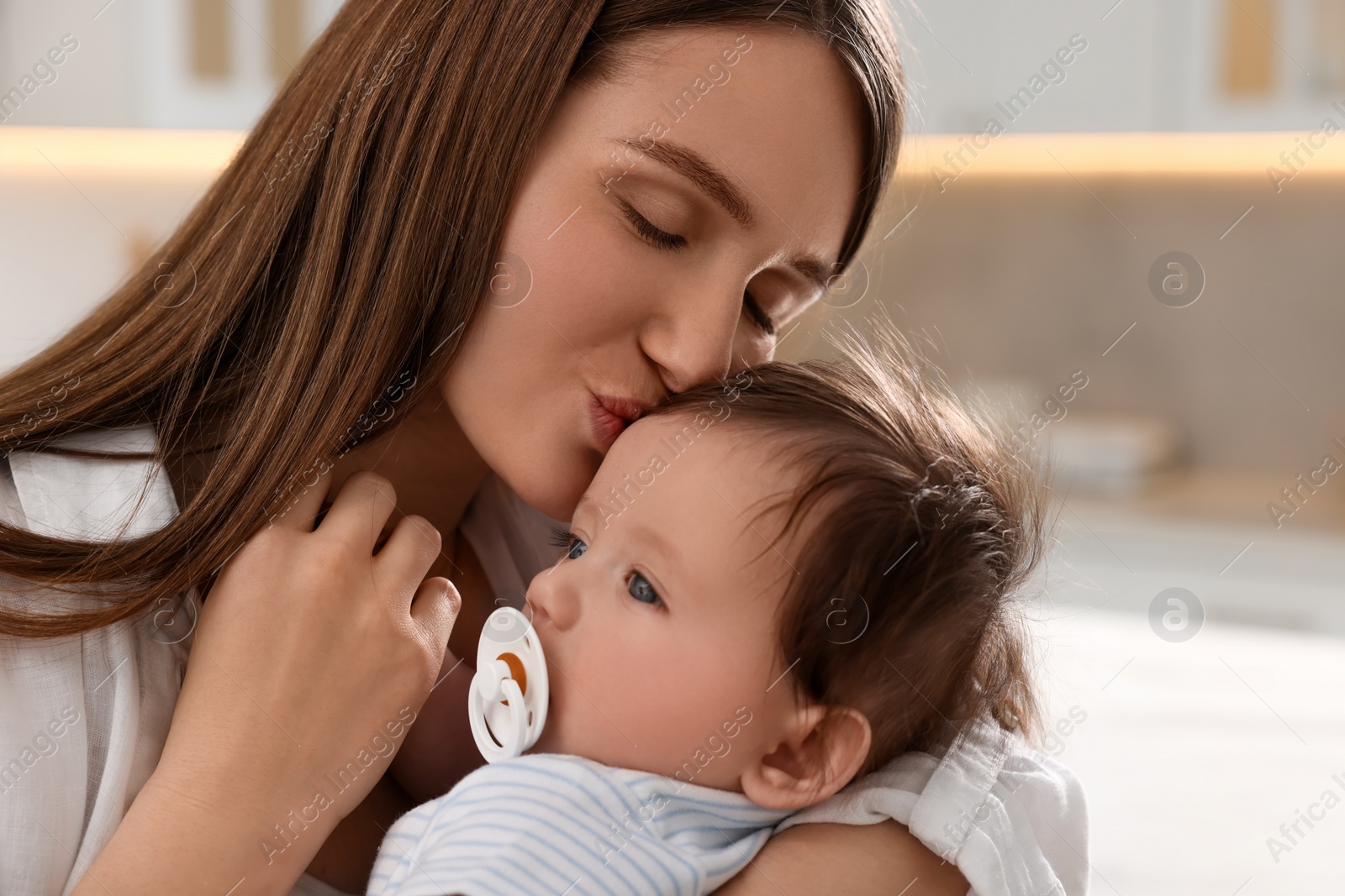 Photo of Happy mother kissing her little baby in kitchen, closeup