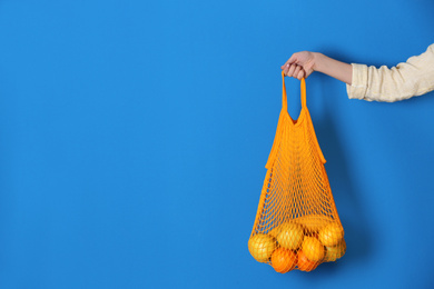 Photo of Woman holding net bag with fruits on blue background, closeup. Space for text