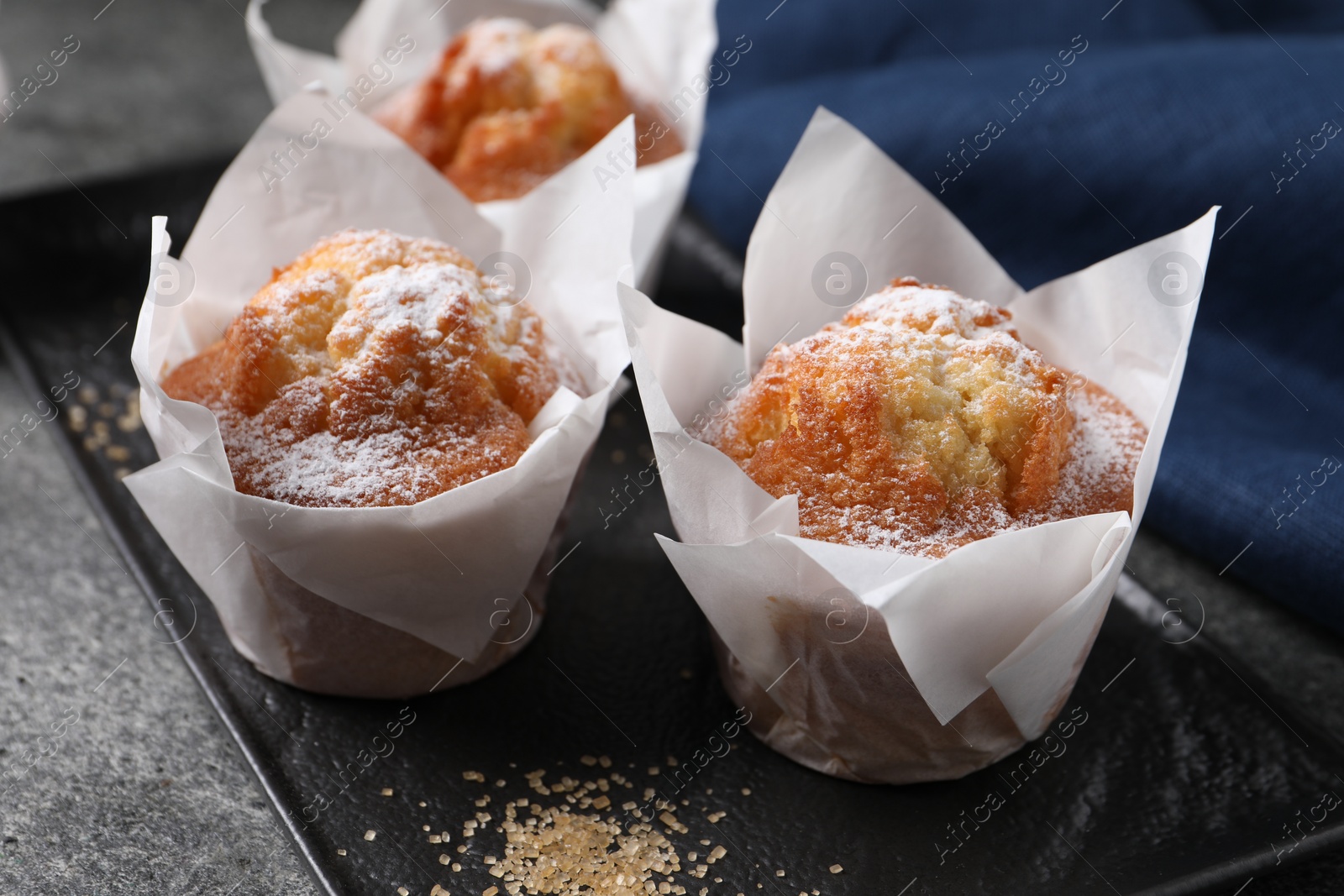 Photo of Delicious muffins with powdered sugar on grey table, closeup