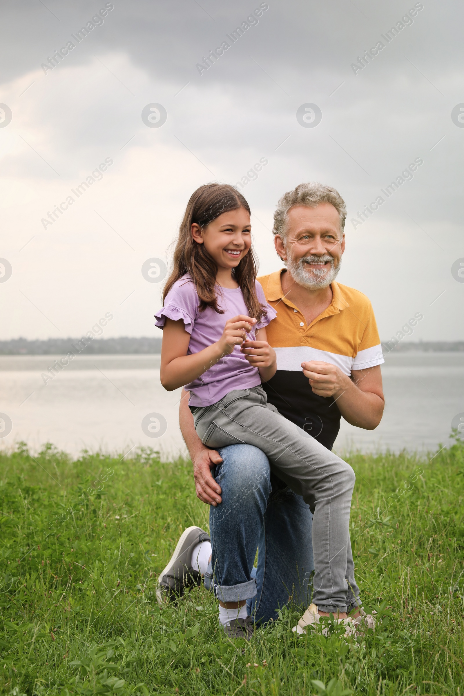 Photo of Little girl and grandfather spending time together near river