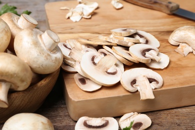 Wooden board with sliced champignon mushrooms on table