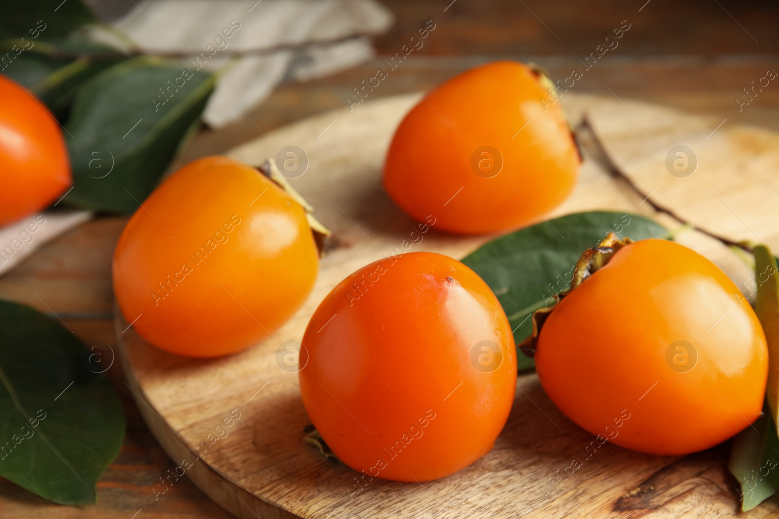 Photo of Delicious fresh persimmons and green leaves on wooden table, closeup