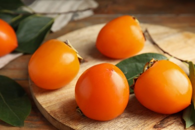 Photo of Delicious fresh persimmons and green leaves on wooden table, closeup