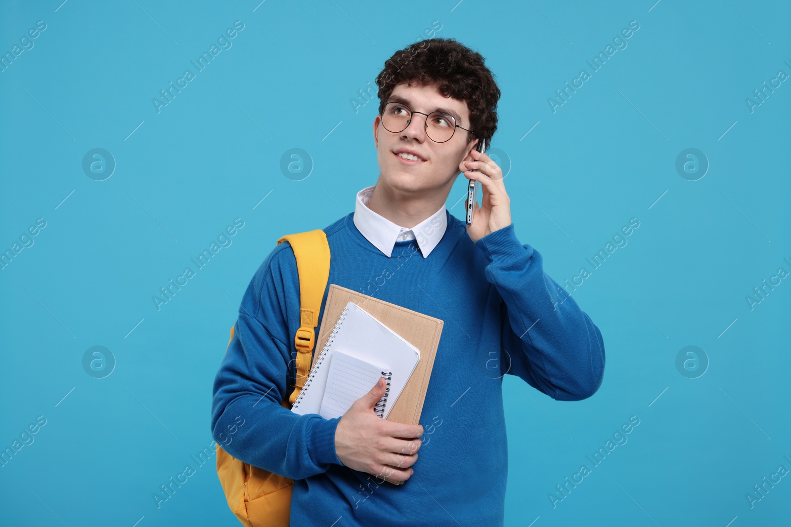 Photo of Portrait of student with backpack and notebooks talking on smartphone against light blue background