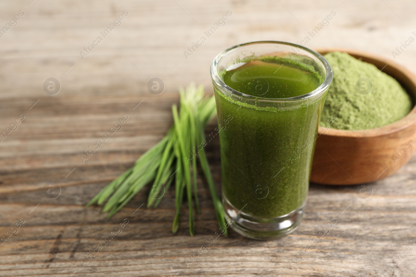 Photo of Wheat grass drink in shot glass on wooden table, closeup. Space for text