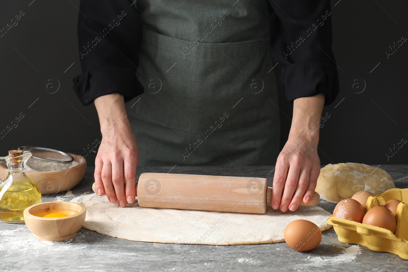 Photo of Woman rolling raw dough at grey table, closeup