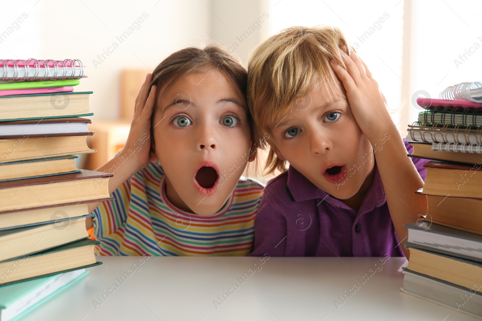 Photo of Emotional little boy and girl at table with books. Doing homework