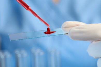 Scientist dripping sample of red liquid onto microscope slide, closeup