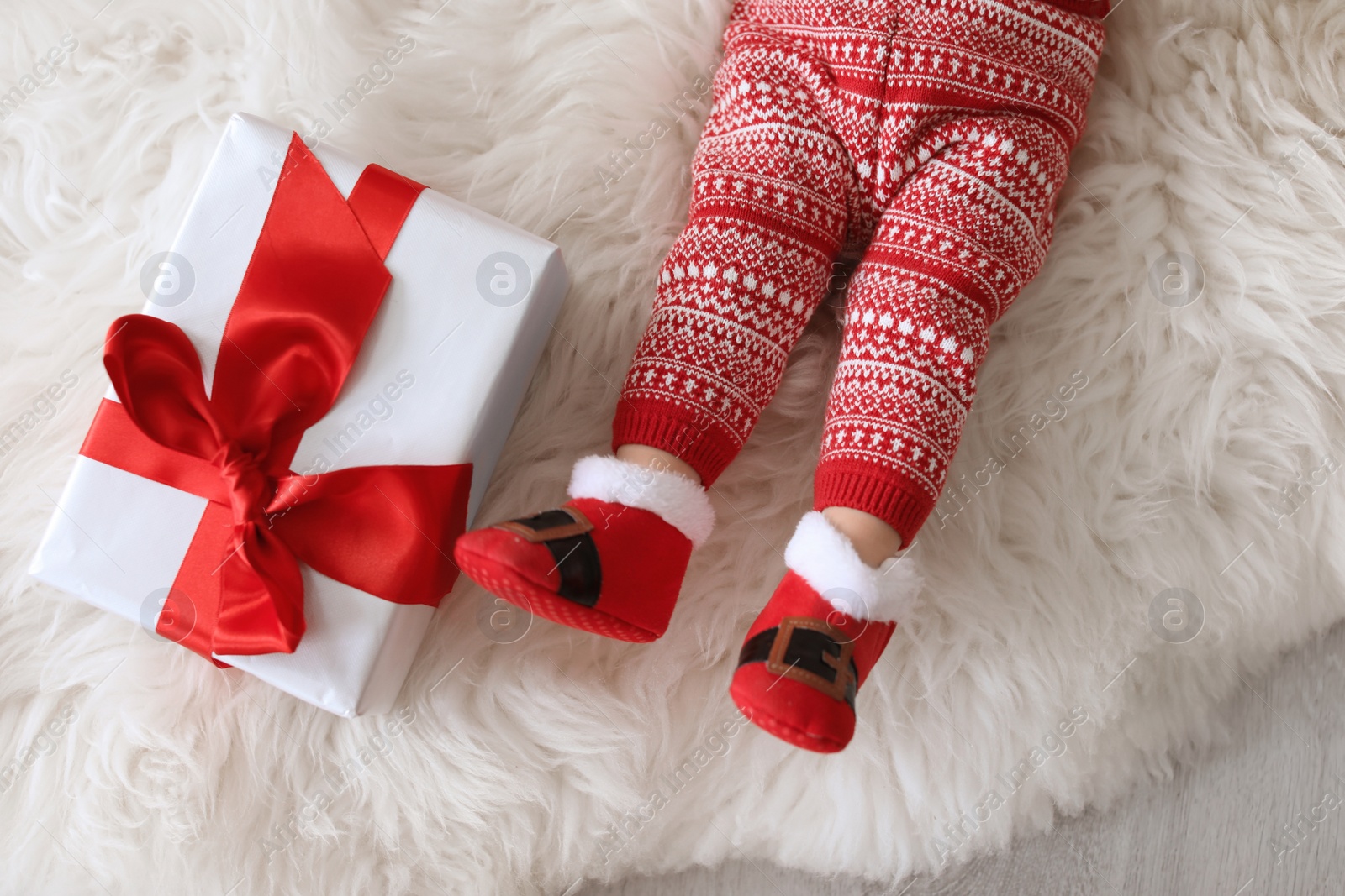 Photo of Cute baby in Christmas costume with gift box on fur rug