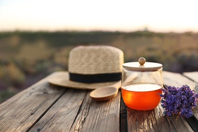 Photo of Jar with fresh honey and lavender flowers on wooden table outdoors. Space for text