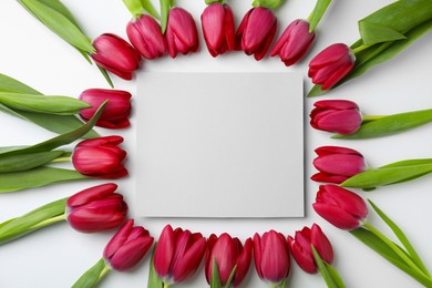 Many beautiful tulips and blank card on white background, flat lay