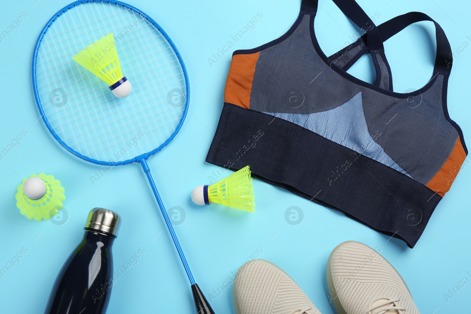 Photo of Rackets, sportswear and bottle on light blue background, flat lay. Playing badminton