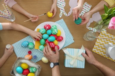 Family with colorful Easter eggs at table, top view