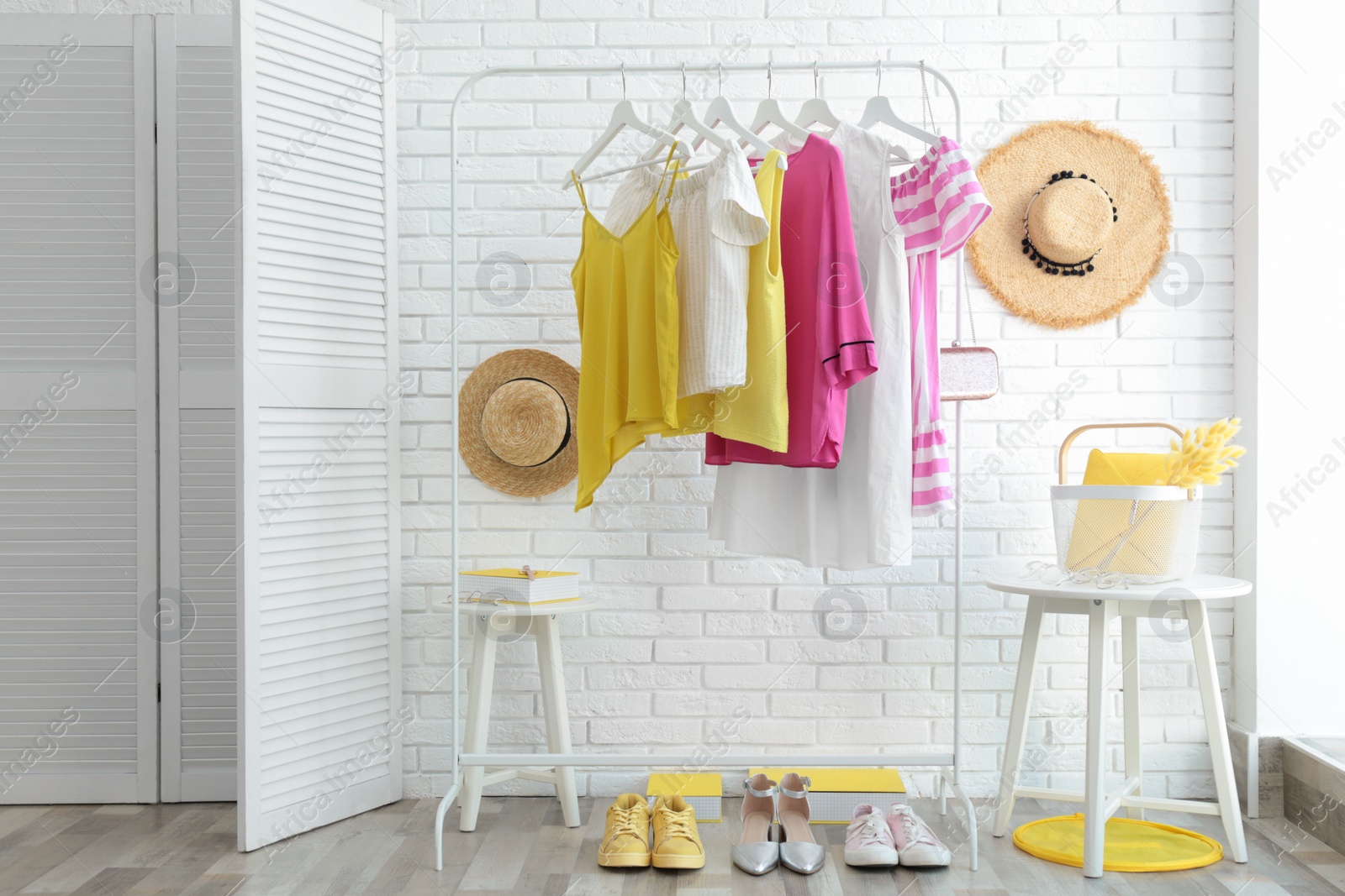 Photo of Wardrobe rack with women's clothes and different shoes at white brick wall in room