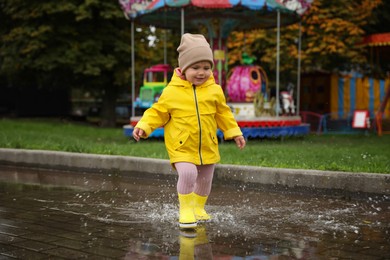 Photo of Cute little girl walking in puddle near carousel outdoors