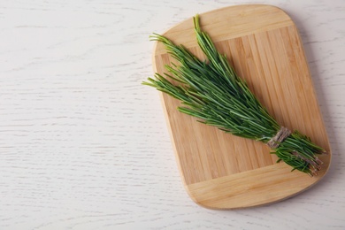 Photo of Board with bundle of fresh rosemary twigs on white wooden background, top view. Space for text