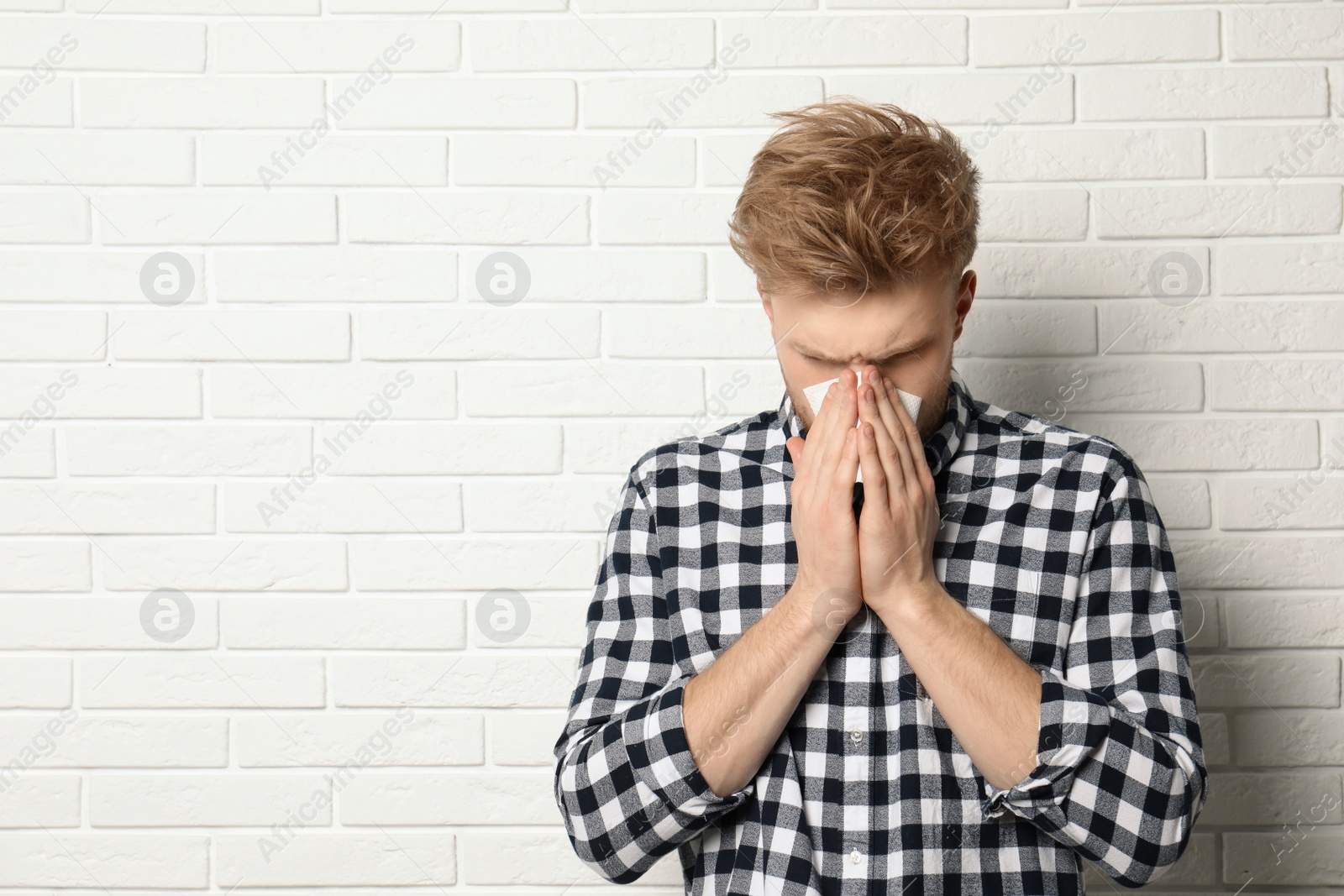 Photo of Handsome young man blowing nose near brick wall. Space for text