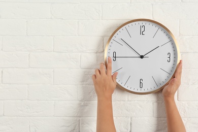 Photo of Woman touching clock on white brick wall, space for text. Time management