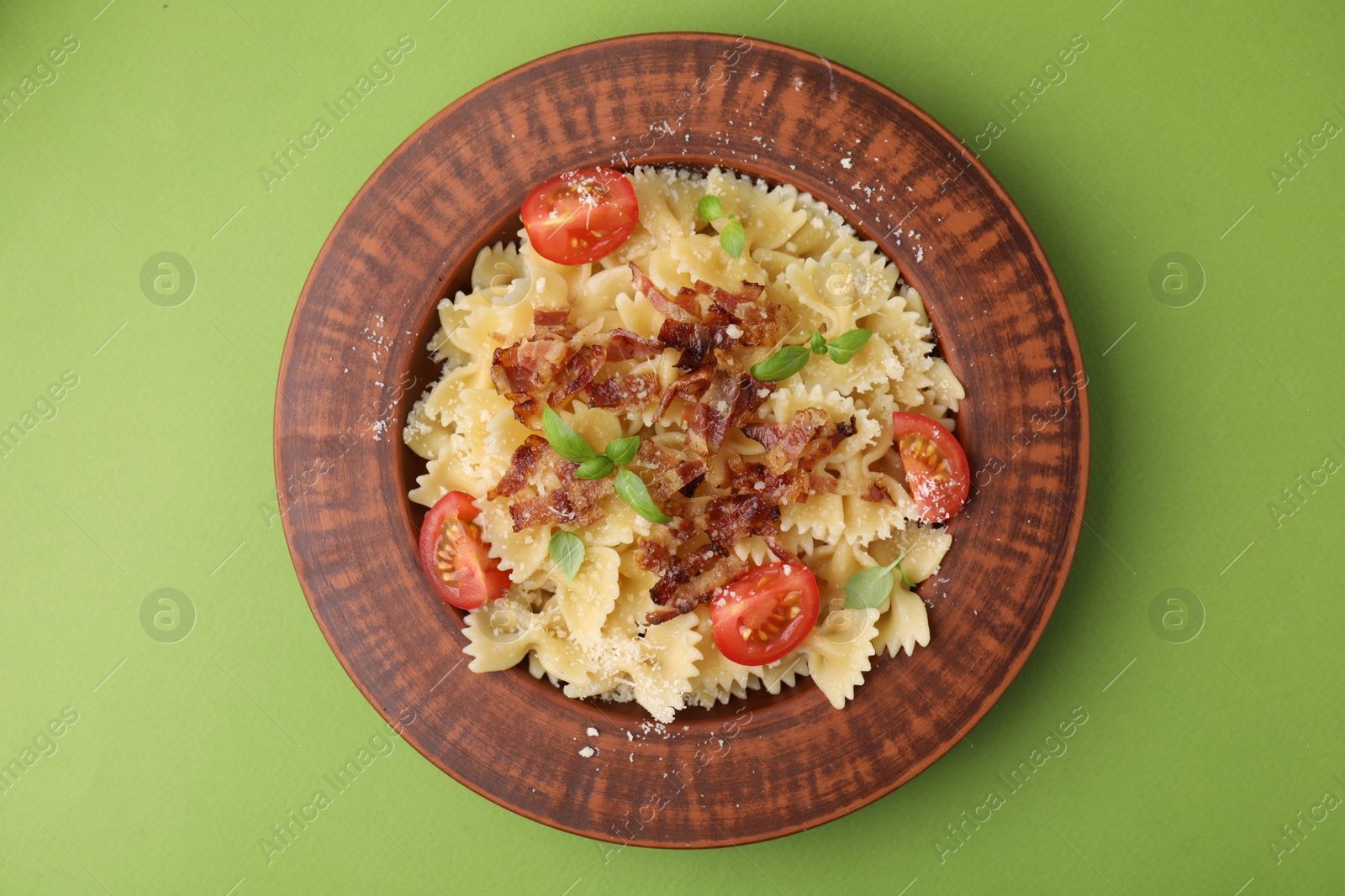 Photo of Tasty pasta with bacon, tomatoes and basil on light green table, top view