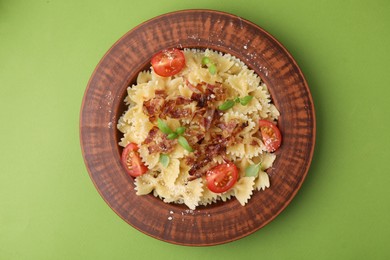 Tasty pasta with bacon, tomatoes and basil on light green table, top view