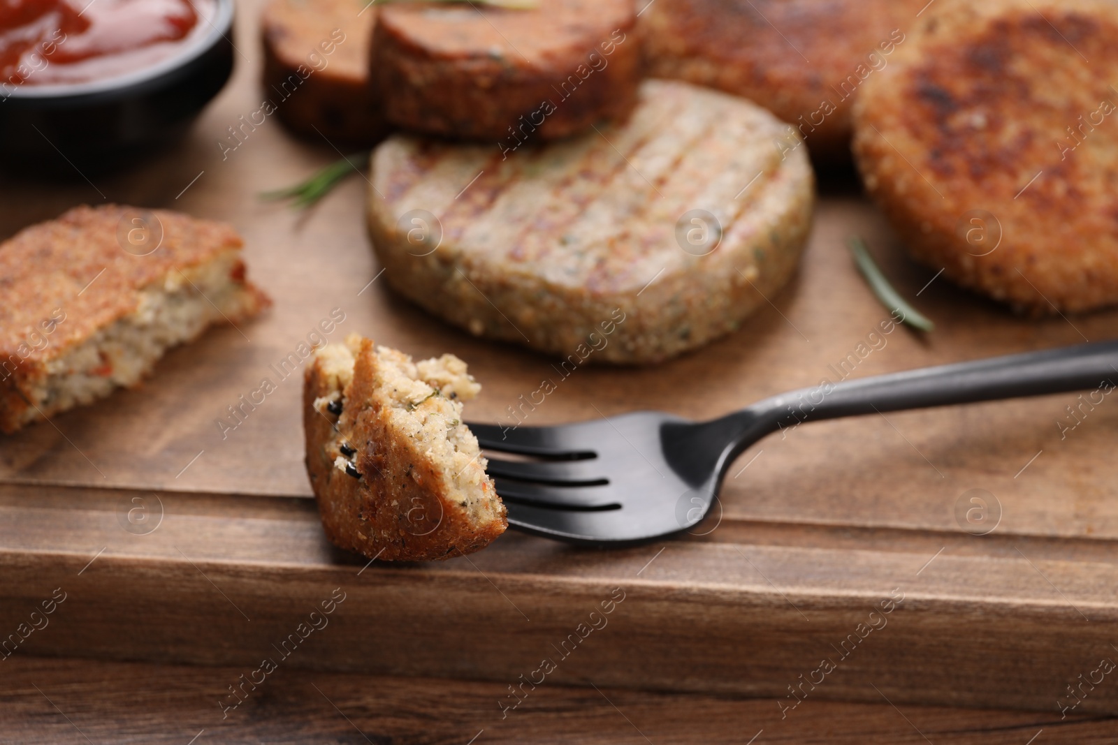 Photo of Fork with piece of delicious vegan cutlet on wooden table, closeup