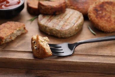 Fork with piece of delicious vegan cutlet on wooden table, closeup