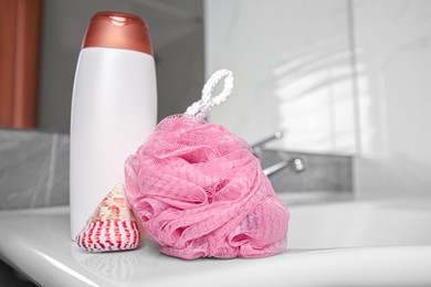 Pink sponge, seashell and shower gel bottle on washbasin in bathroom, closeup. Space for text