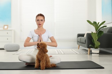 Photo of Young woman practicing yoga on mat with her cute dog at home. Space for text