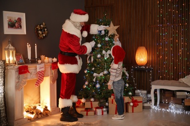 Little child with Santa Claus putting star on top of Christmas tree at home