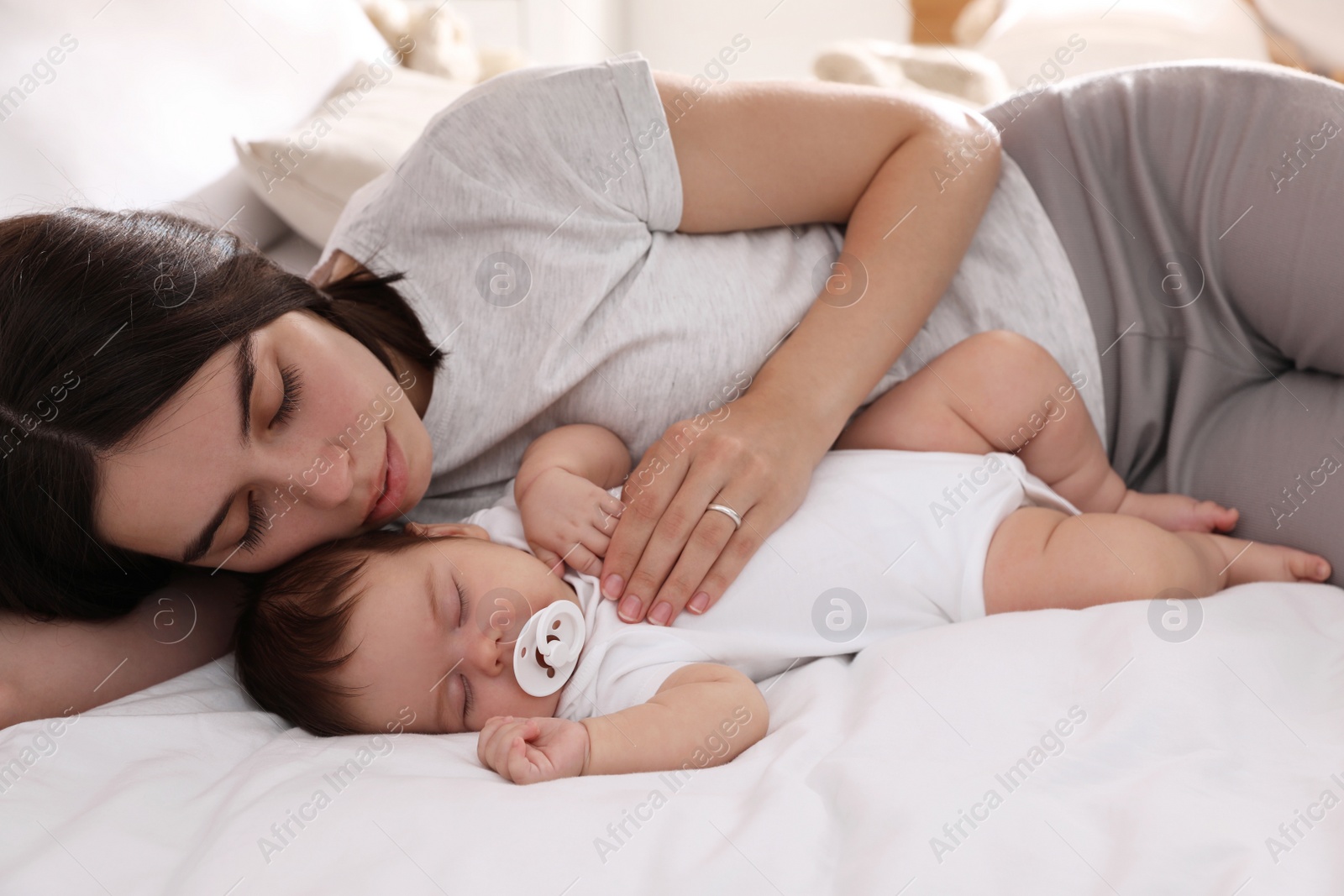 Photo of Young mother resting near her sleeping baby on bed at home