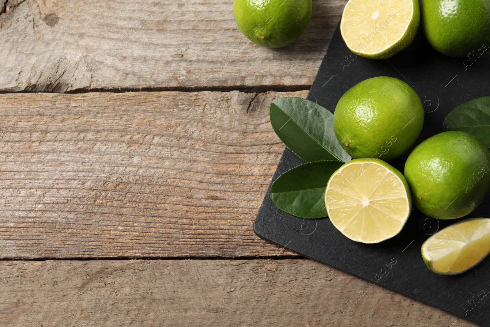 Photo of Fresh limes and green leaves on wooden table, top view. Space for text