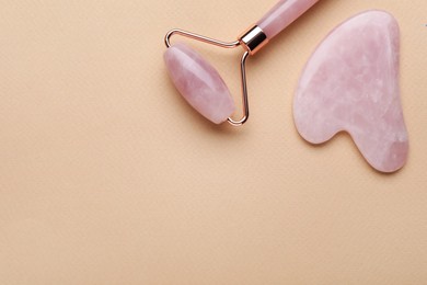 Gua sha stone and face roller on beige background, flat lay. Space for text