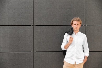 Portrait of handsome young man leaning to wall outdoors, space for text