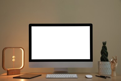Photo of Comfortable workplace with blank computer display on desk and plant near beige wall. Space for text